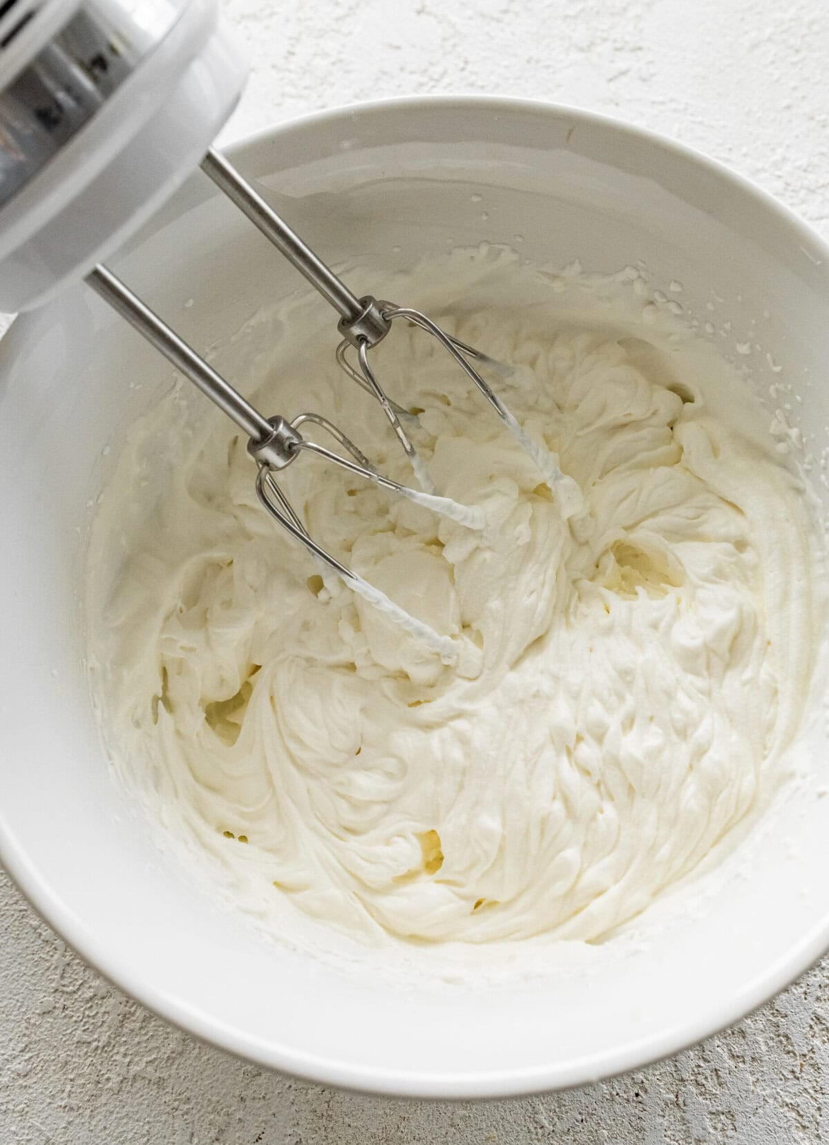 Beaters in a bowl of whipped powdered sugar and heavy cream. 