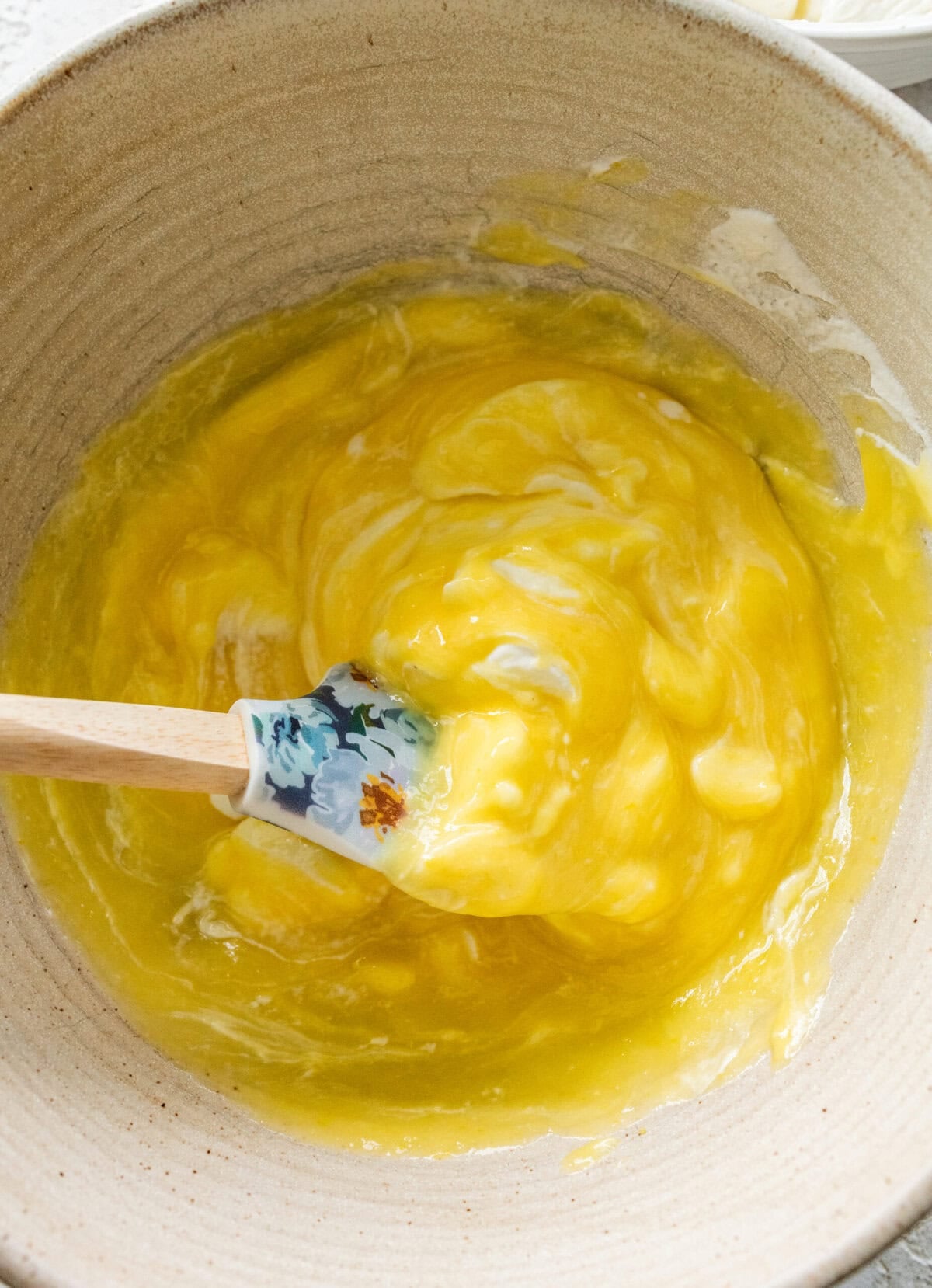 Whipped cream and lemon curd being folded together by a spatula in a bowl.