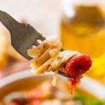 A fork holding up one bite of italian poached fish over a plate of more.