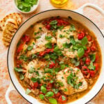 Italian poached fish in a skillet with garnish and more ingredients nearby.