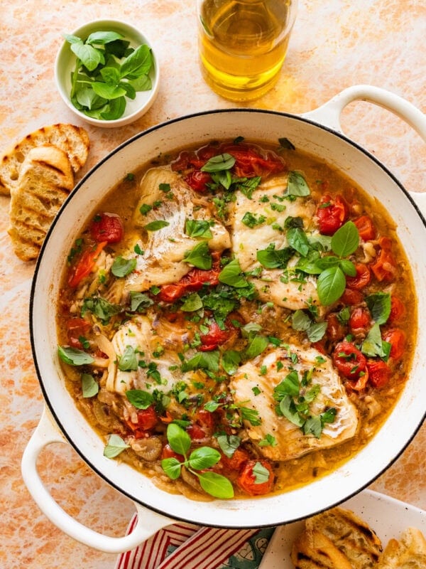 Italian poached fish in a skillet with garnish and more ingredients nearby.