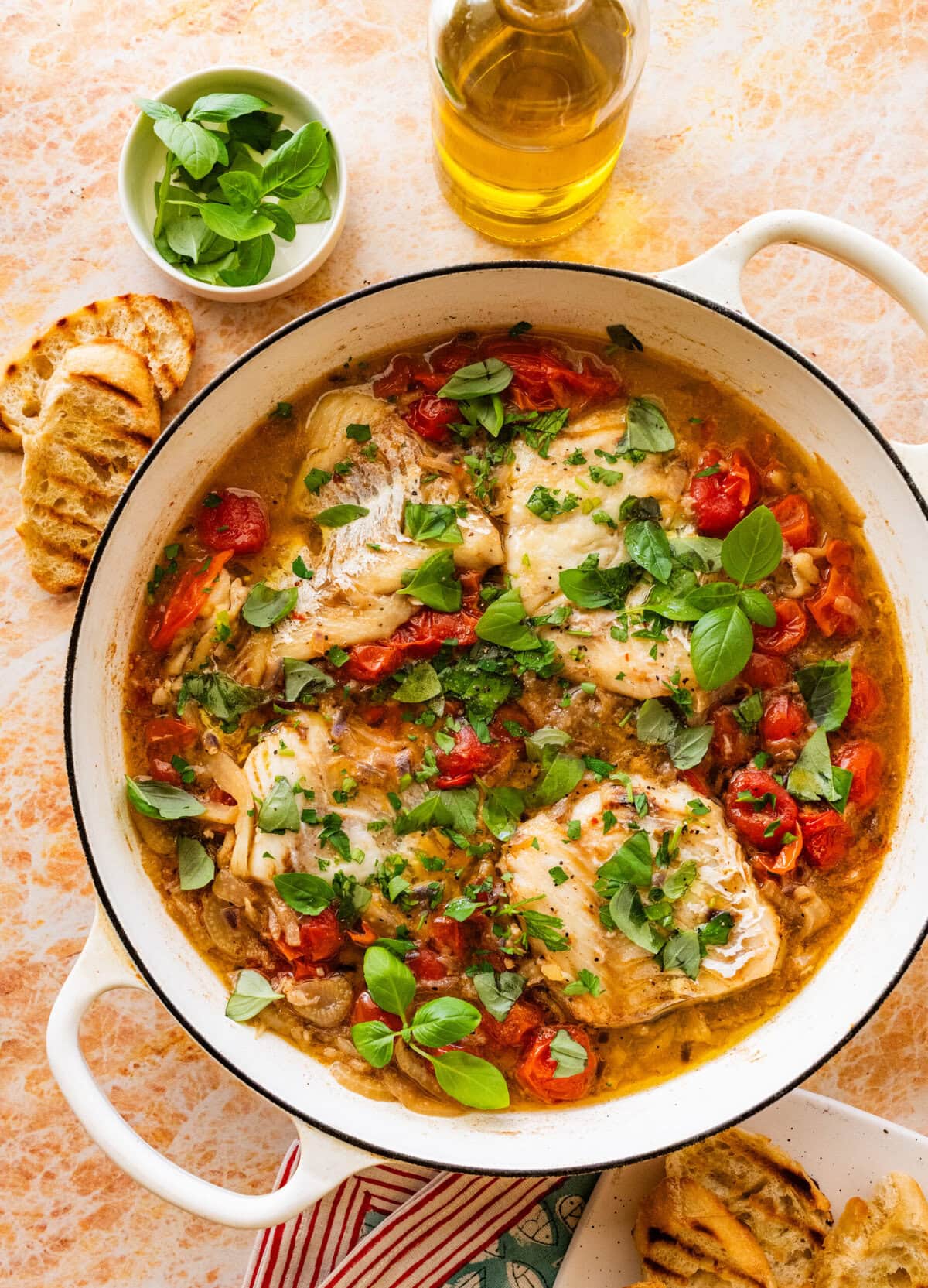 Italian poached fish in a skillet with garnish and more ingredients nearby.