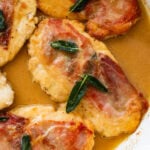 four chicken saltimbocca breasts in a pan after cooking, garnished with sage.