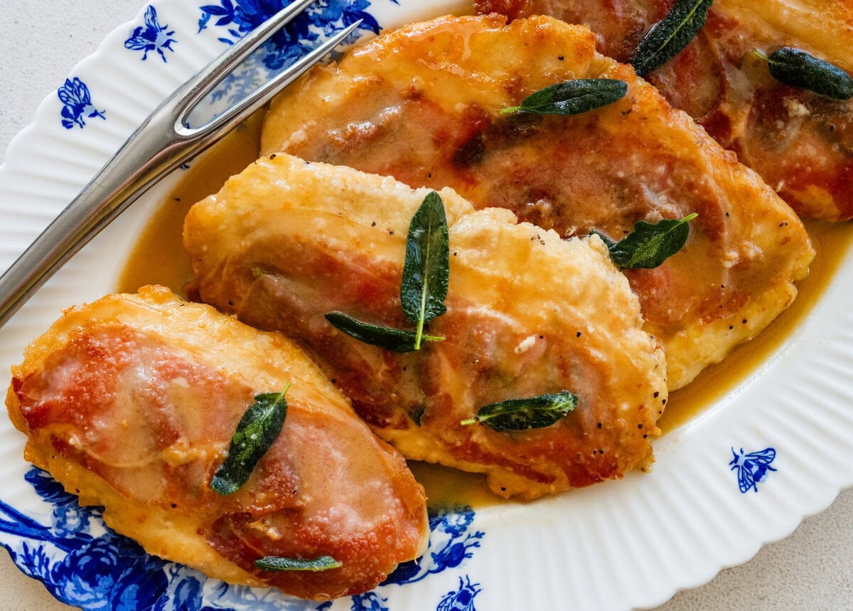 four chicken saltimbocca breasts on a plate after cooking, garnished with sage.