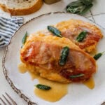 two pieces of chicken saltimbocca on a plate, garnished with sage, with more ingredients nearby.