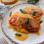 two pieces of chicken saltimbocca on a plate, garnished with sage, with more ingredients nearby.