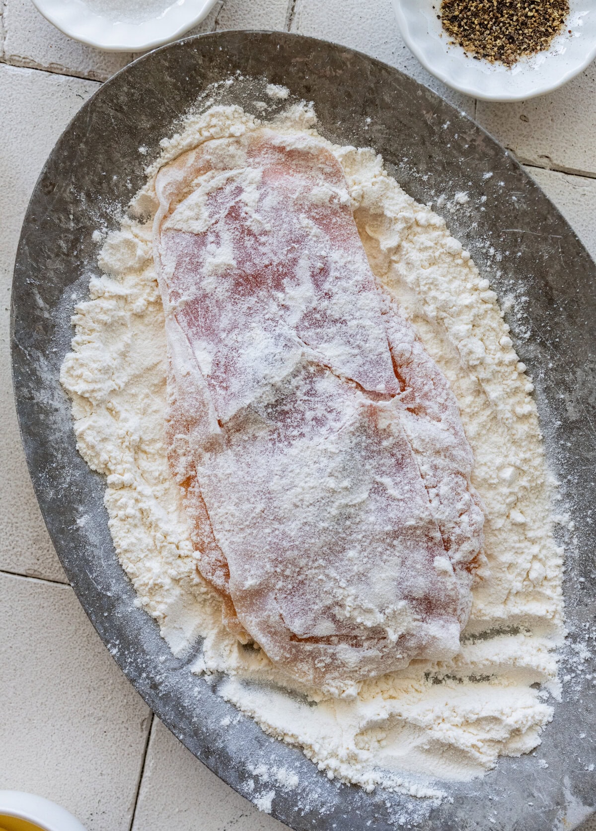 a plate of flour with a piece of chicken being coated.
