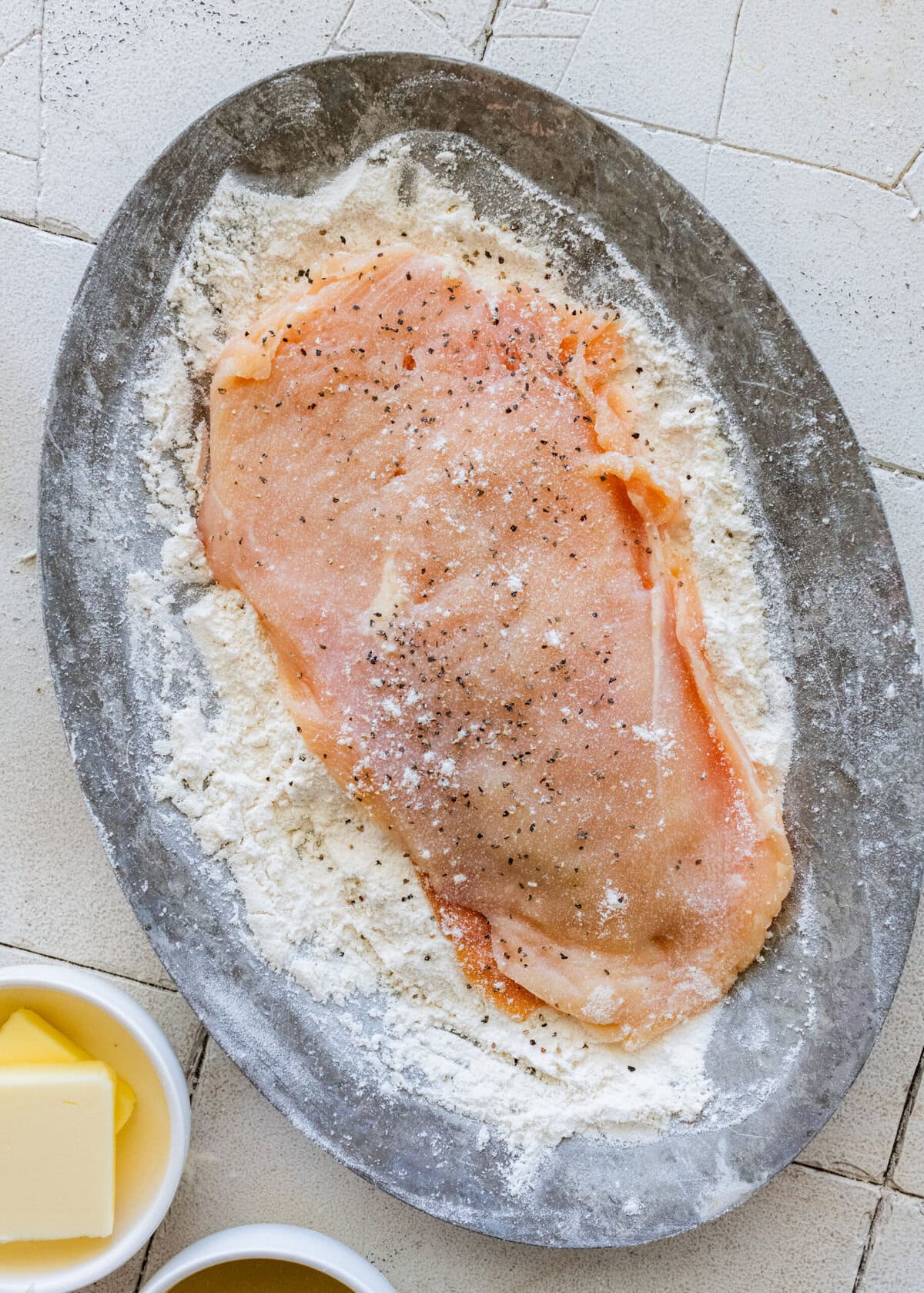 chicken breast laying in the flour, with the non-floured side being seasoned.