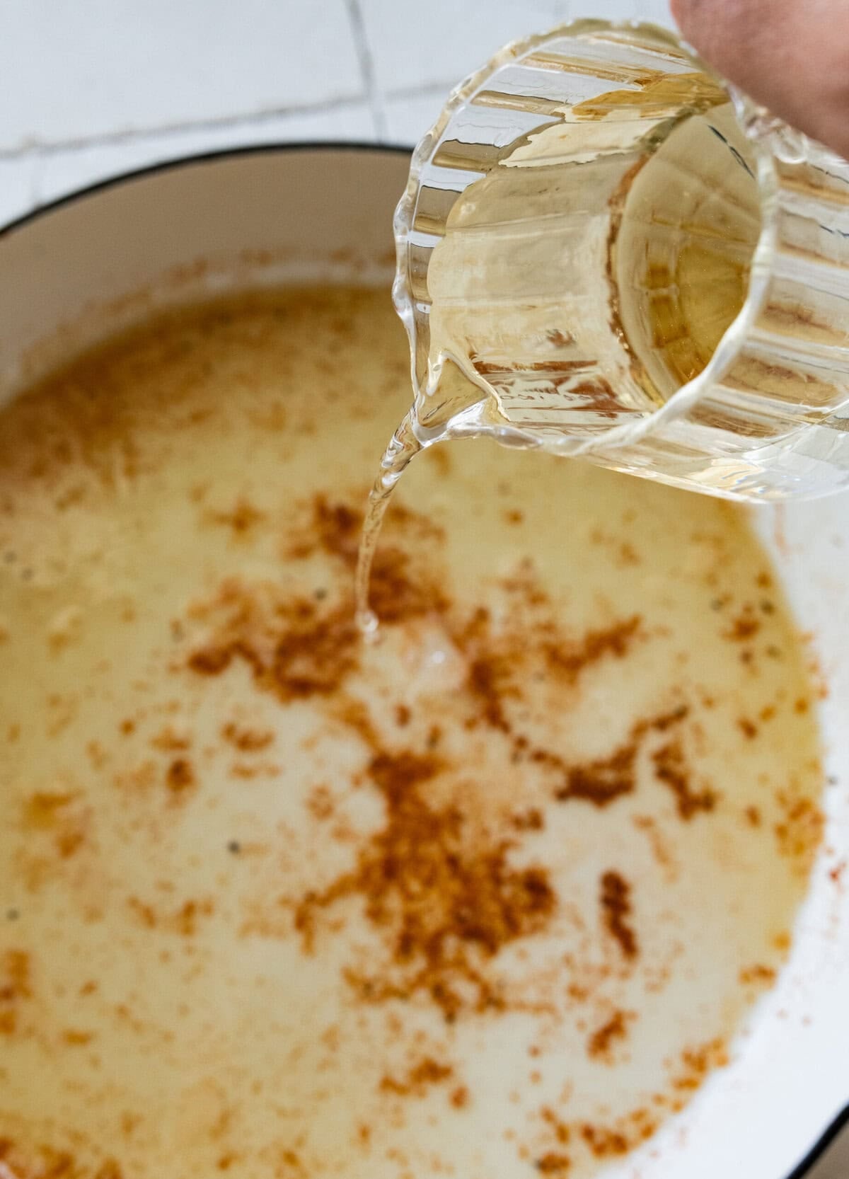 pouring white wine into the pan once the chicken is removed.