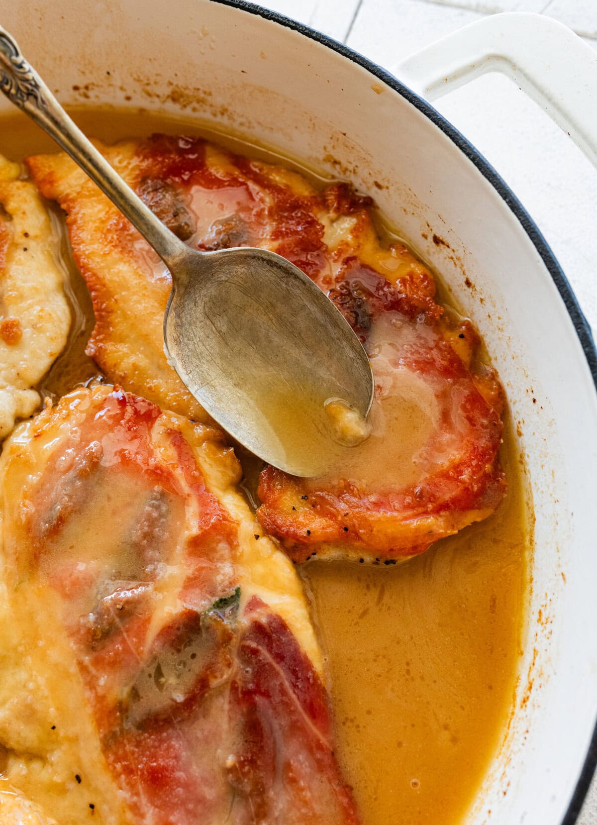 a spoon pouring some of the sauce over the chicken in the pan.