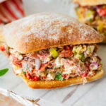 two chopped italian sandwiches after assembling, with a glass of water between them.