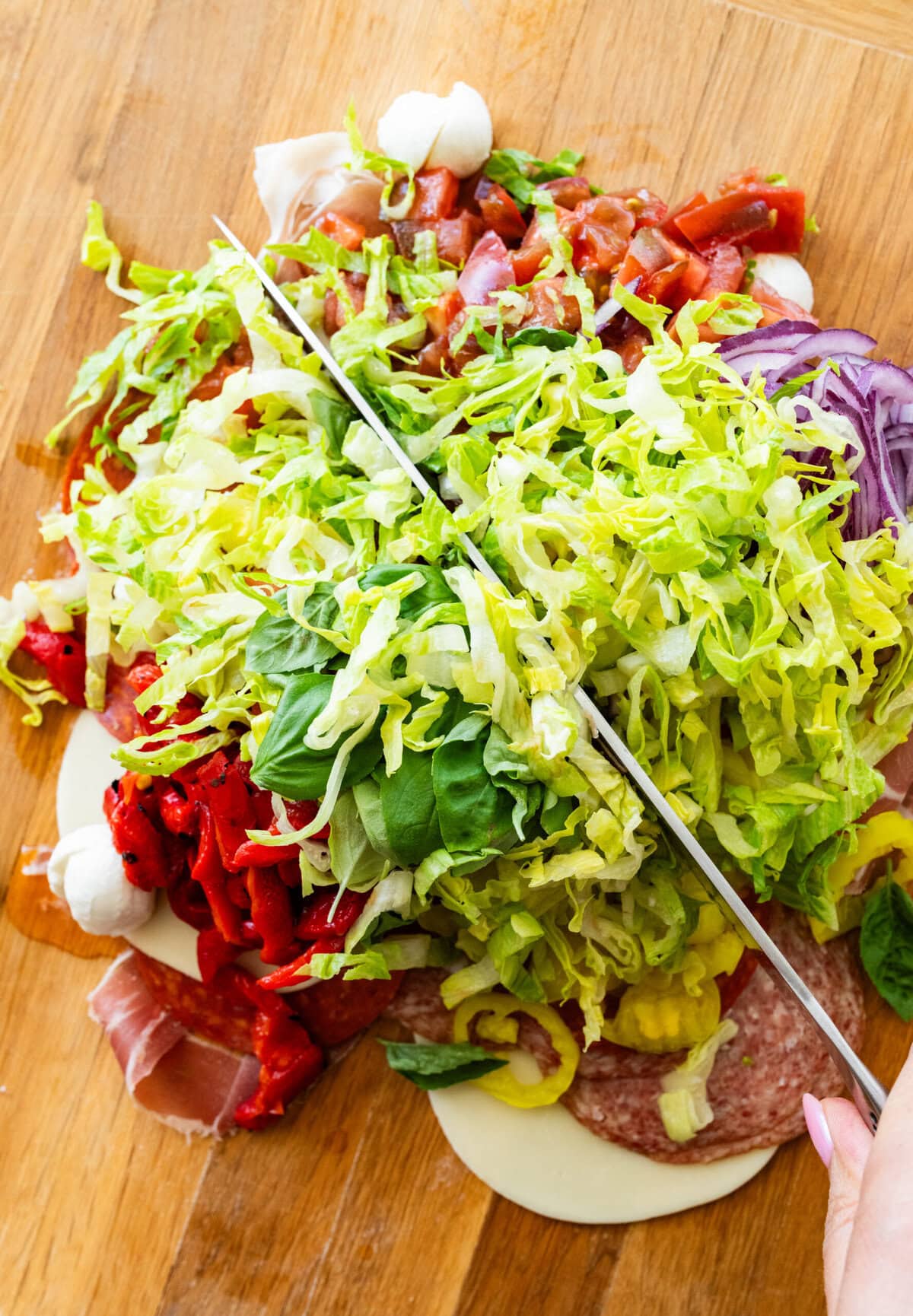 the rest of the sandwich topping ingredients added to the cutting board with a knife starting to chop everything up.