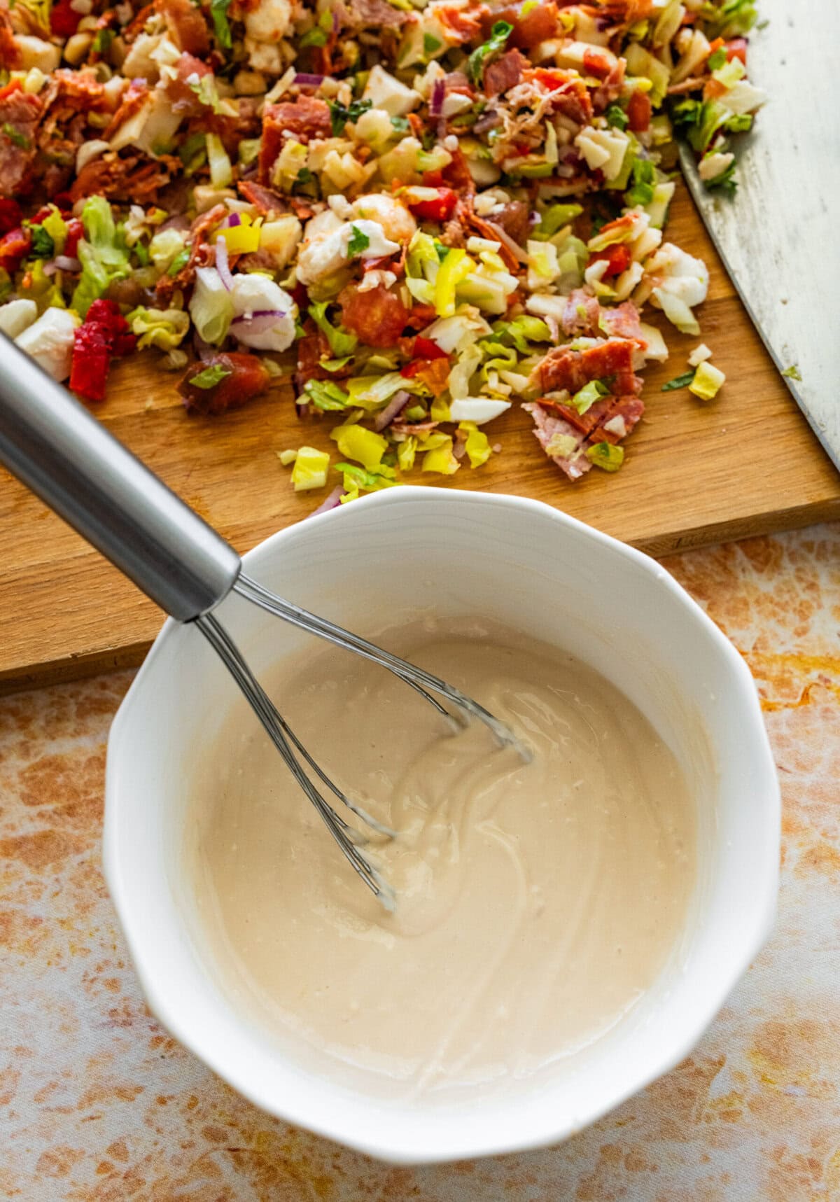 a bowl of the dressing ingredients being whisked next to the cutting board of chopped ingredients.