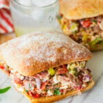 two chopped italian sandwiches after assembling, with a glass of water between them.