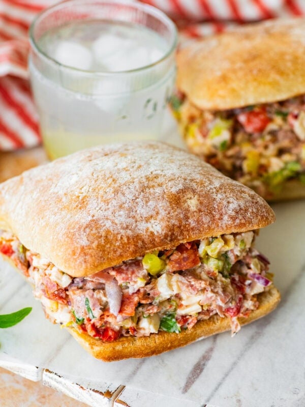 two chopped italian sandwiches after assembling, with a glass of water between them.