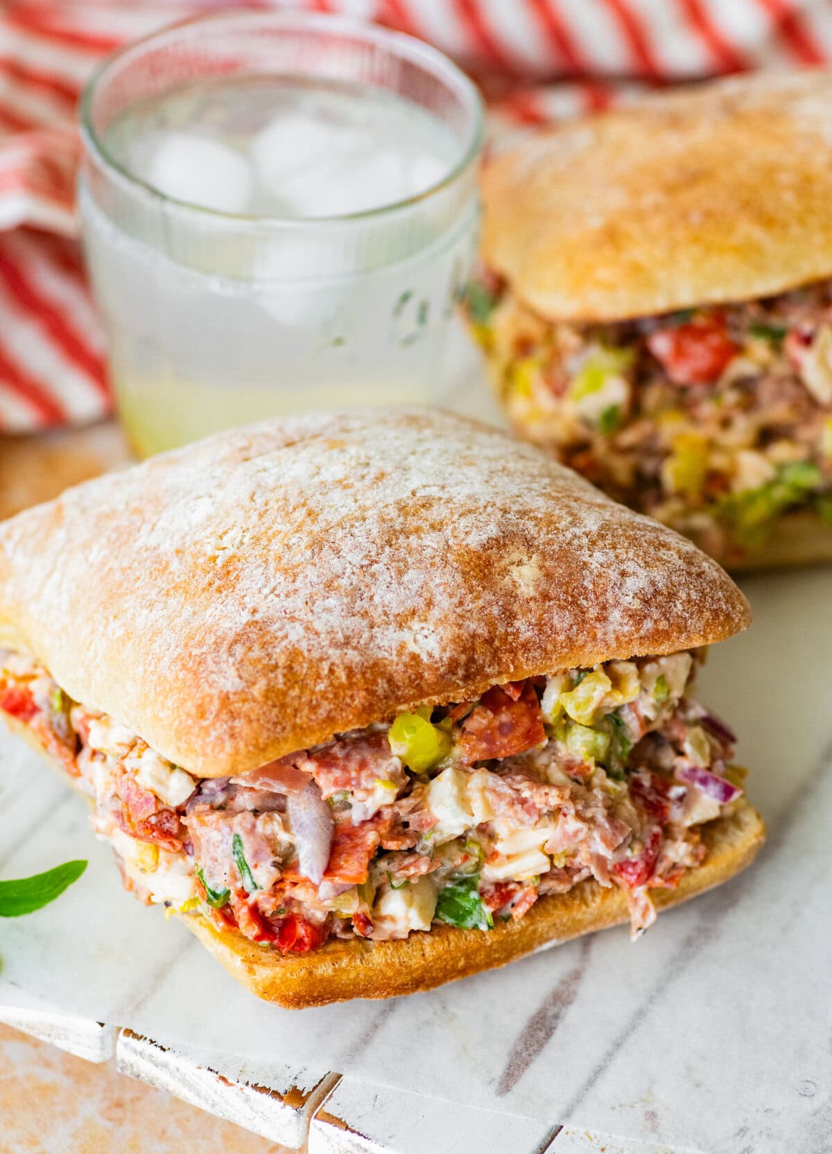 two chopped italian sandwiches after assembling, with a glass of water between them.
