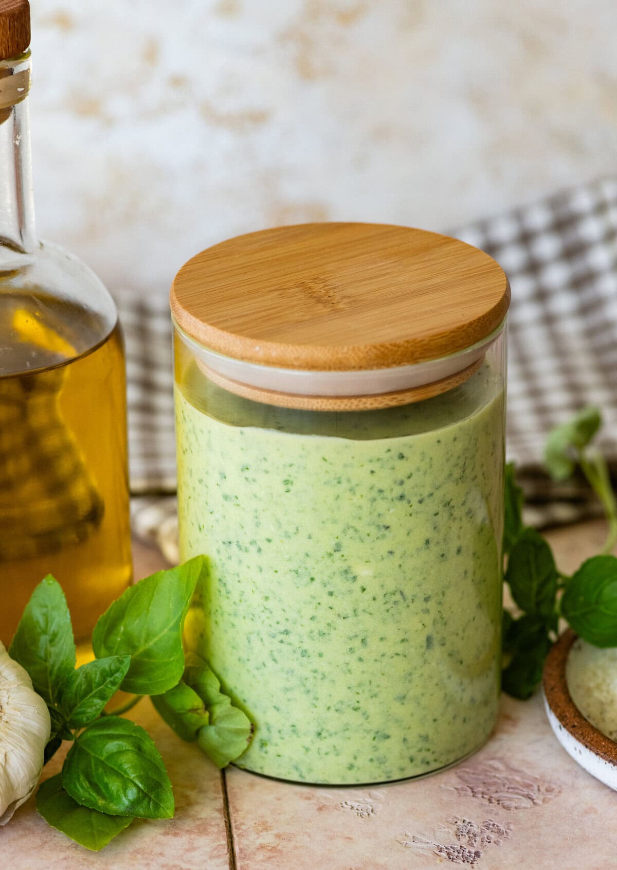 a clear jar of creamy pesto sauce with more ingredients nearby.
