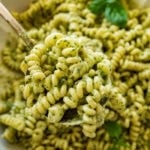 creamy pesto pasta in a shallow dish, garnished with fresh basil, with a fork holding up some.