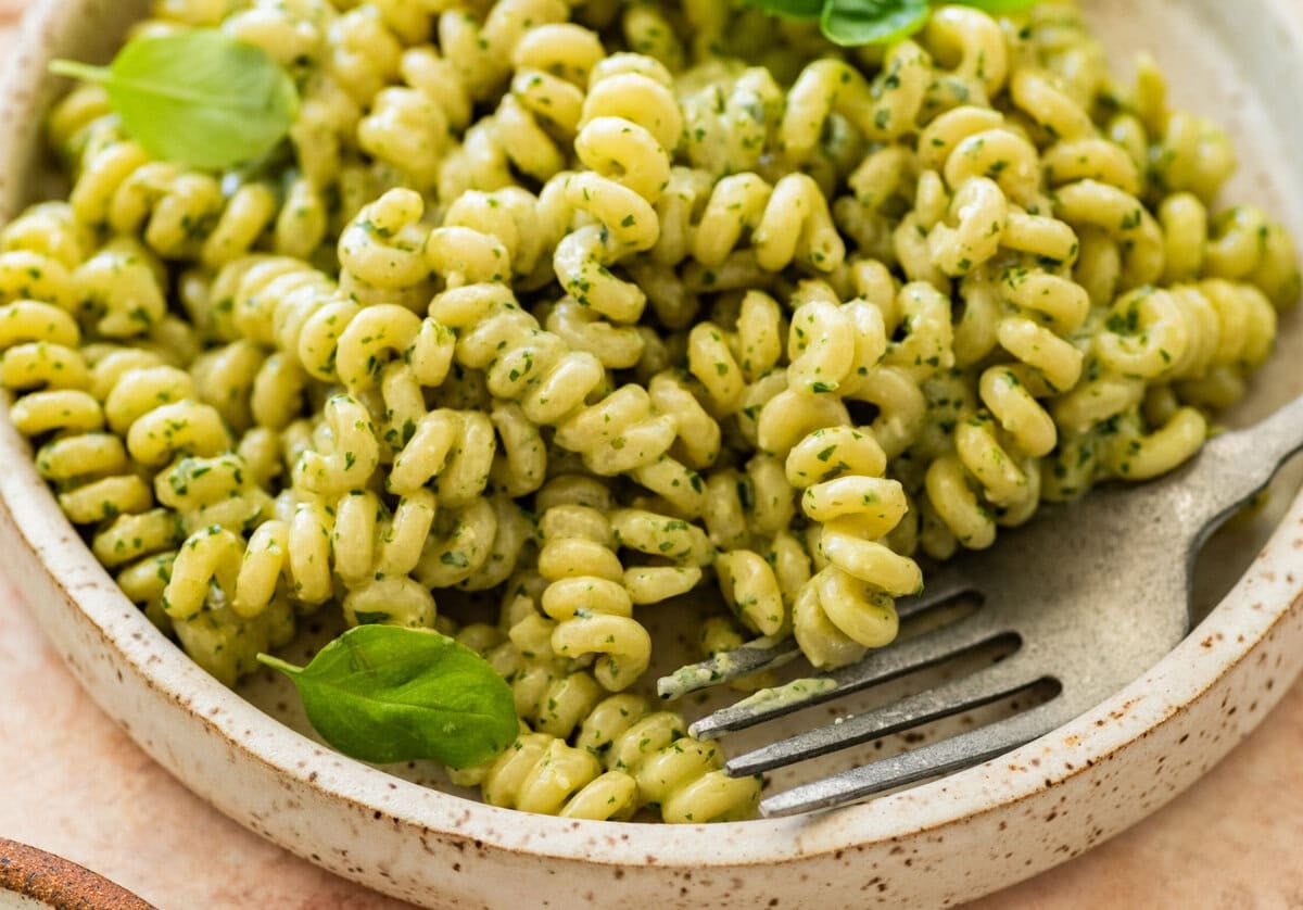 creamy pesto pasta in a shallow dish, garnished with fresh basil, with a fork resting on the plate.