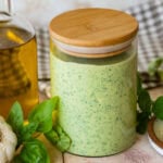 a clear jar of creamy pesto sauce with more ingredients nearby.