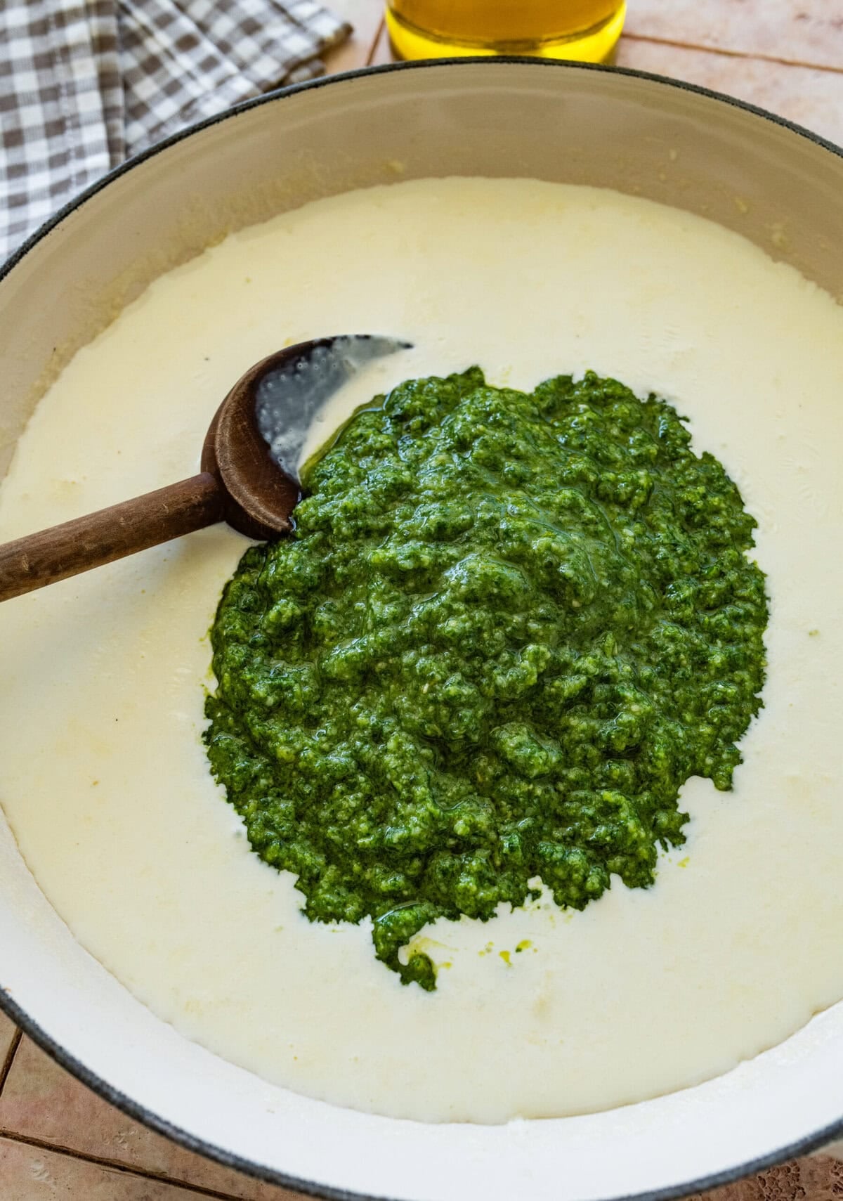 a pot of heavy cream and milk, with the basil pesto added to the stop and a spoon resting inside.