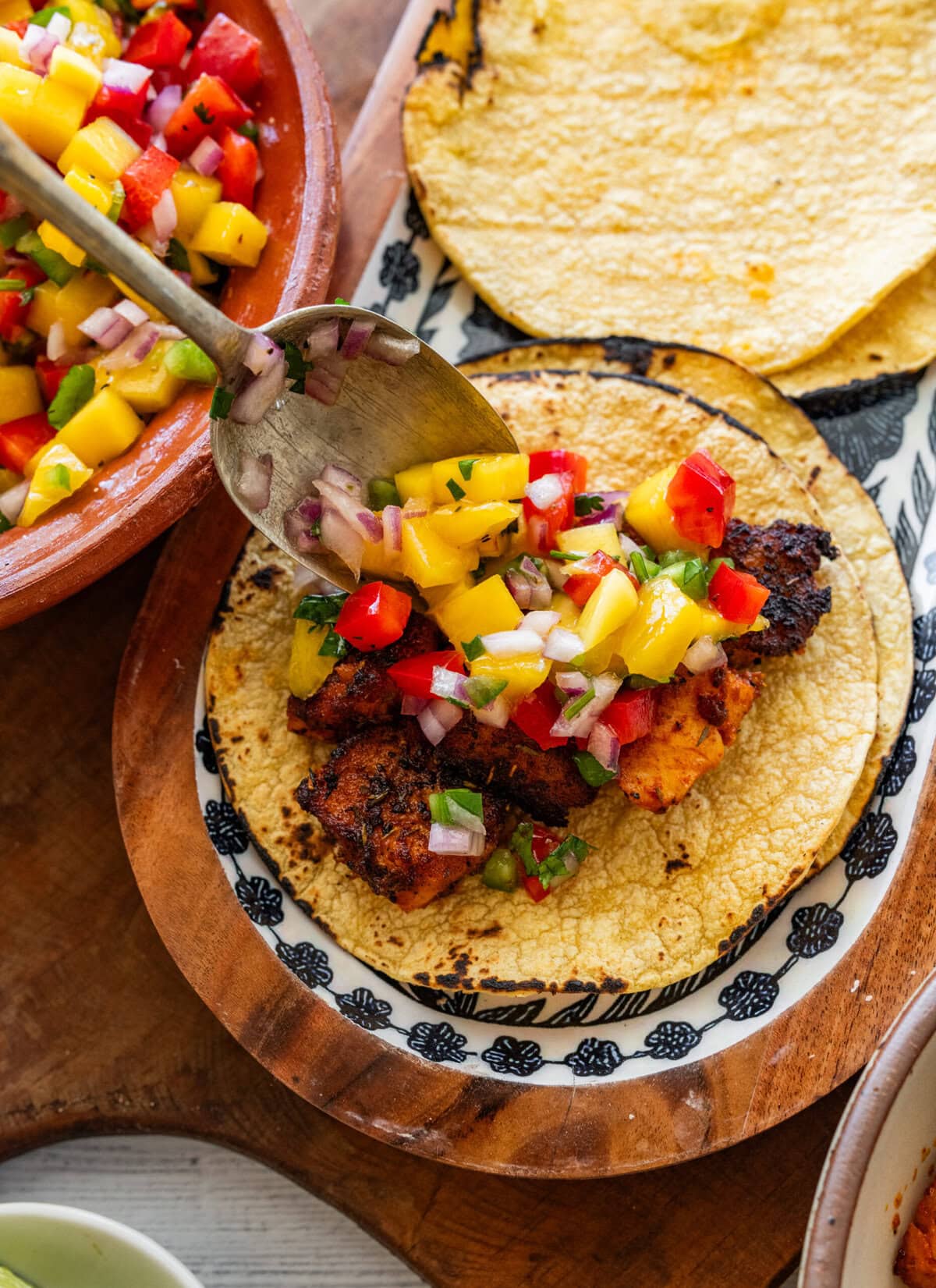 a spoonful of mango salsa being poured onto a taco.