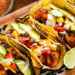 3 fish tacos with toppings, placed on a tray with more ingredients to make the recipe nearby.