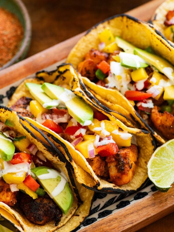 3 fish tacos with toppings, placed on a tray with more ingredients to make the recipe nearby.