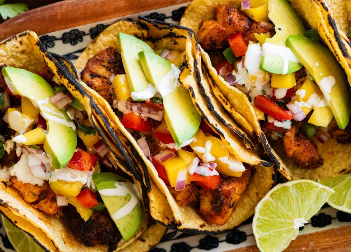 3 fish tacos with toppings, placed on a tray with more ingredients to make the recipe nearby.