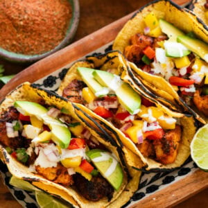 3 fish tacos with toppings, placed on a tray with more ingredients to make the recipe nearby.