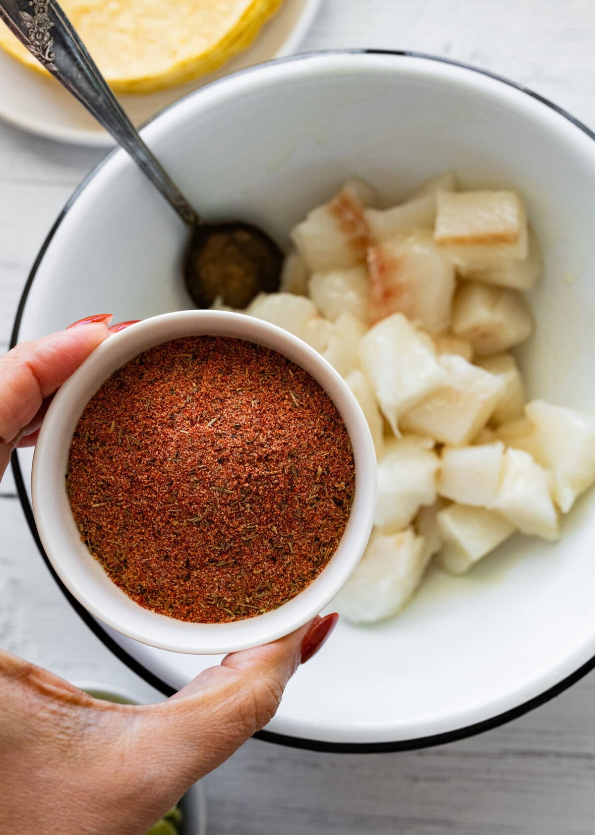 a bowl of blackened seasoning being held over a bowl of cod.