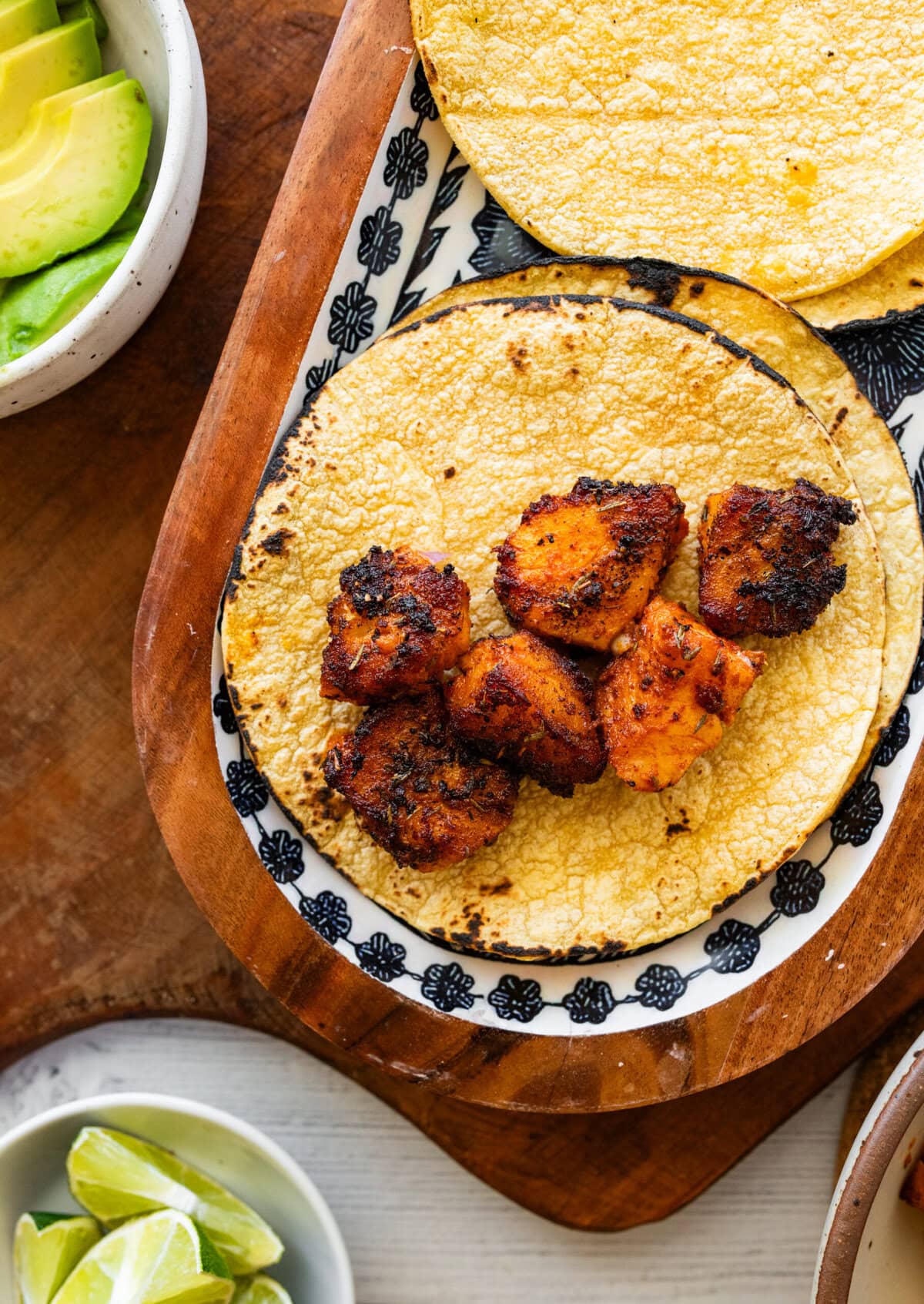 a corn tortilla laid out flat with another nearby, with fish placed in the center and more taco ingredients nearby.