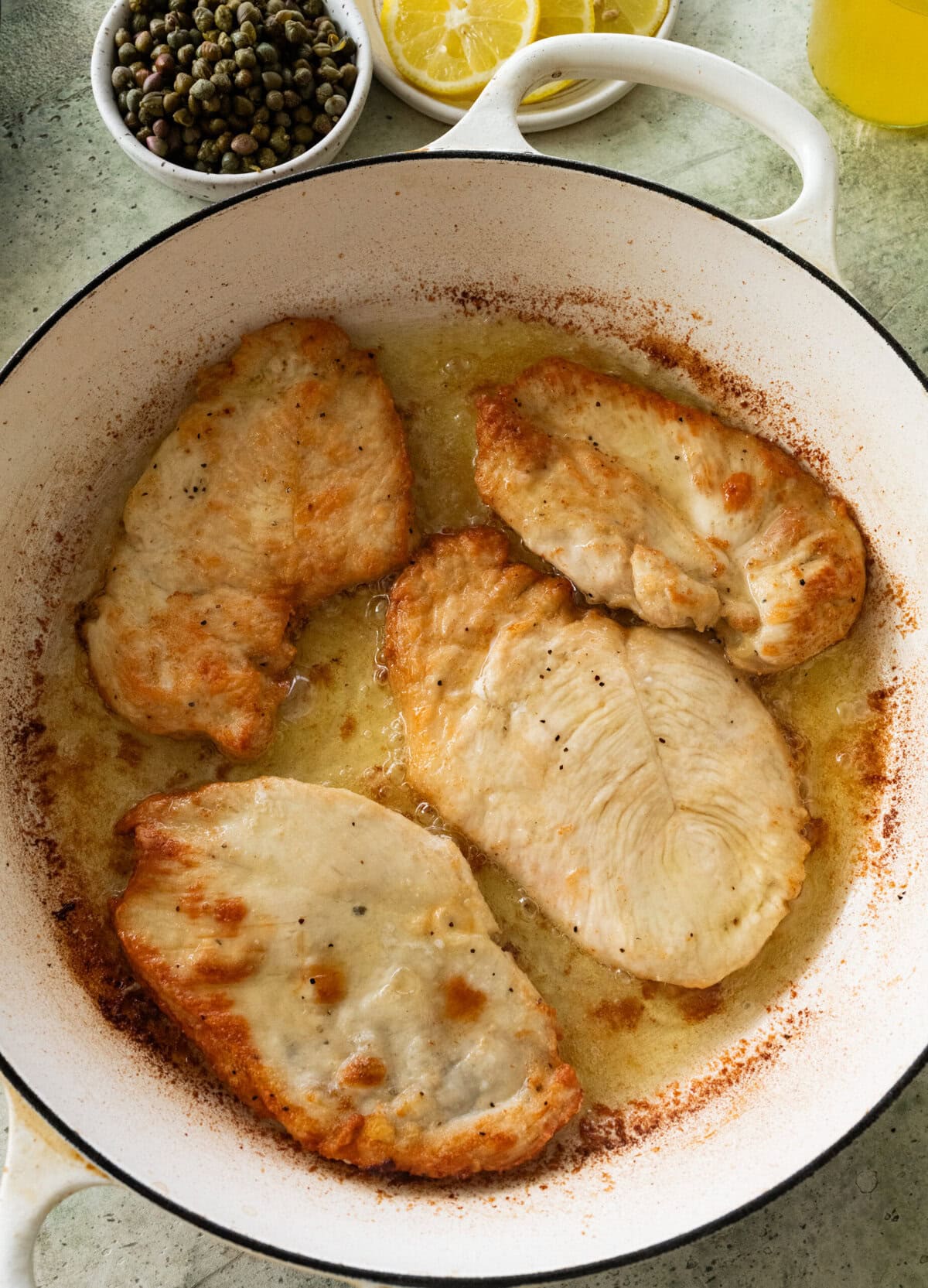 Flour-coated chicken in a skillet with oil.