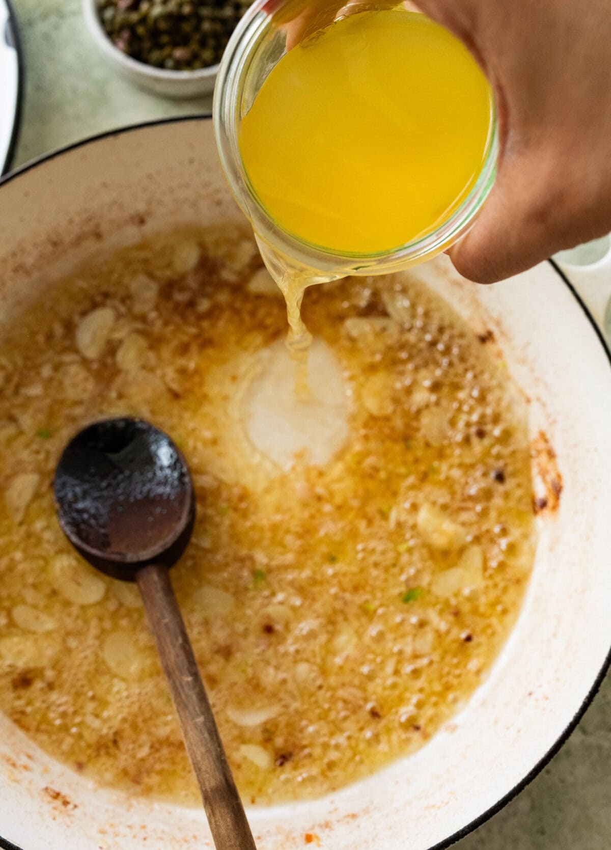 Chicken removed from the skillet that now contains the garlic, shallots, and butter, with broth being poured in to deglaze.