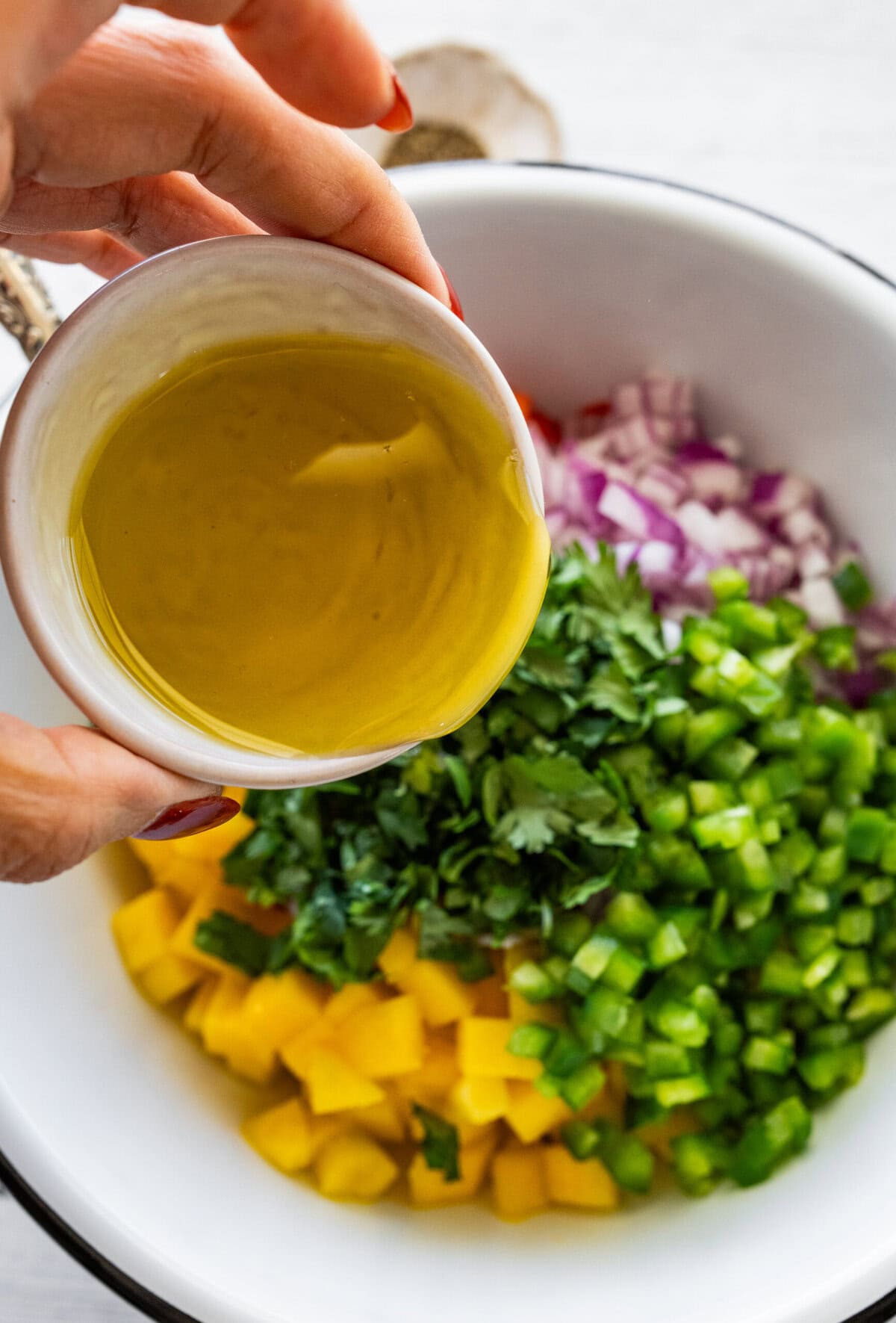 a small bowl of olive oil being poured over the mango salsa ingredients.