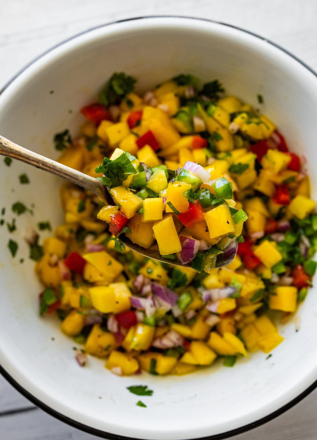 a bowl of fully combined mango salsa with a spoon holding up some.