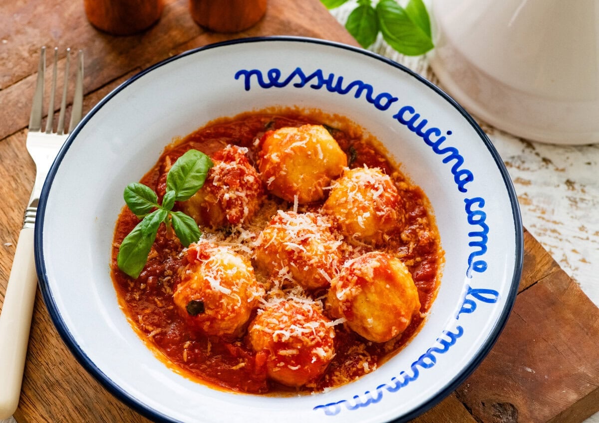 Ricotta gnudi in a bowl with sauce and basil.