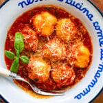 Ricotta gnudi in a bowl with sauce, garnish, and a fork.