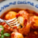 Ricotta gnudi in a bowl with sauce, garnish, and a fork holding up a bite.