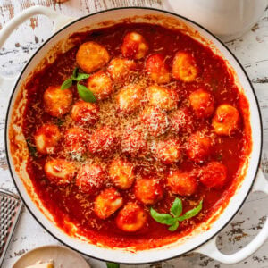 Ricotta gnudi in a skillet after cooking with sauce and garnish.