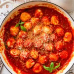 Ricotta gnudi in a skillet after cooking with sauce and garnish.