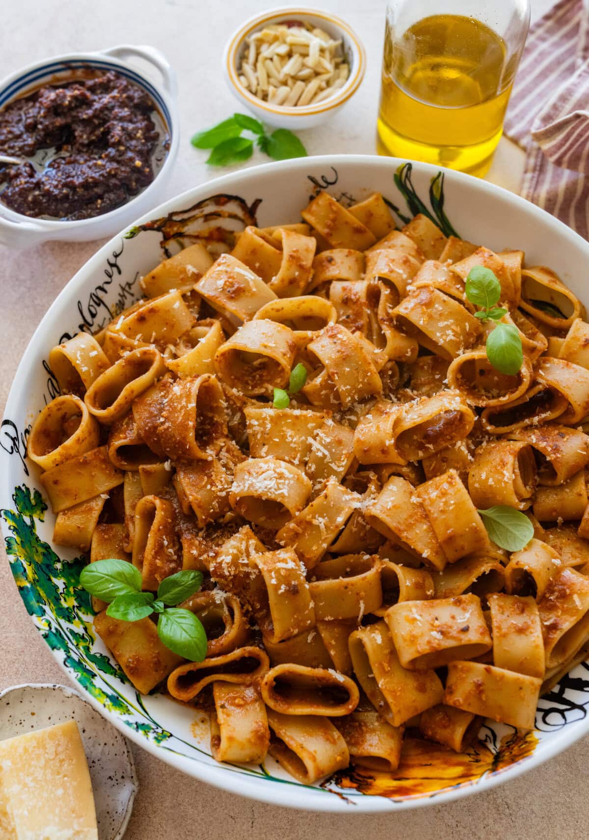 A bowl of sun-dried tomato pesto pasta with garnish, and more ingredients nearby.