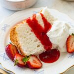 slice of angel food cake with strawberry sauce, whipped cream, and fresh strawberries.