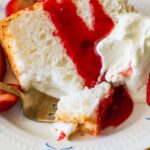 forkful of angel food cake with strawberry sauce on a plate.