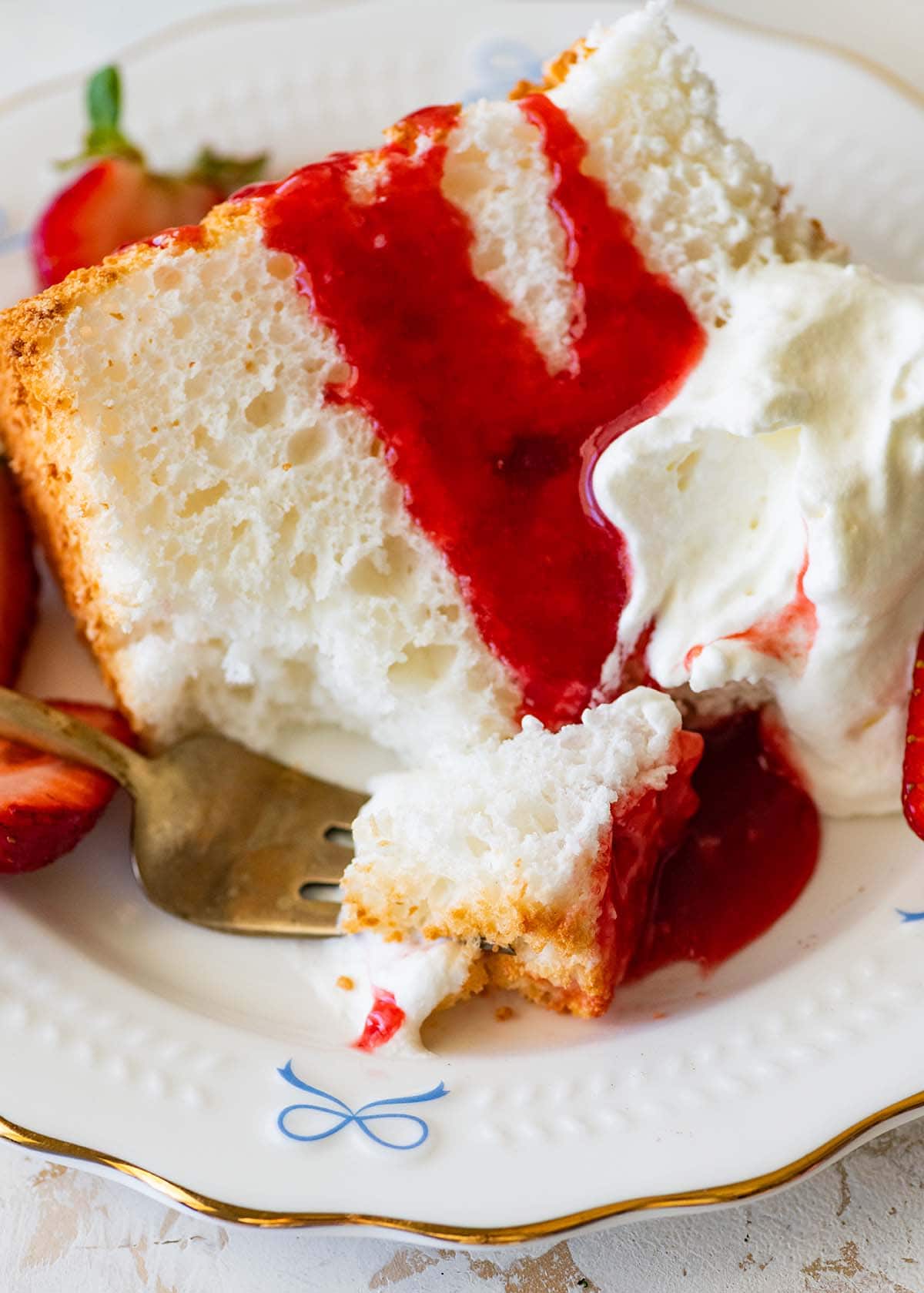forkful of angel food cake with strawberry sauce on a plate.