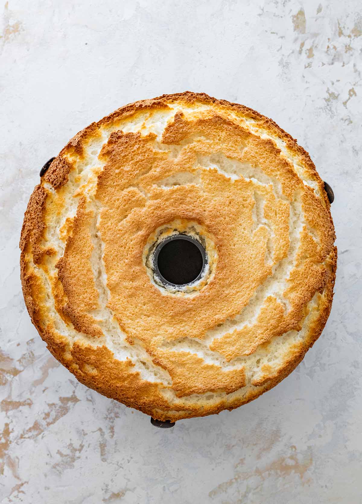 baked angel food cake in a tube pan on a marble countertop.