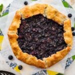blueberry galette on two squares of parchment paper with fresh blueberries.