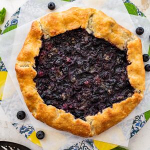 blueberry galette on two squares of parchment paper with fresh blueberries.