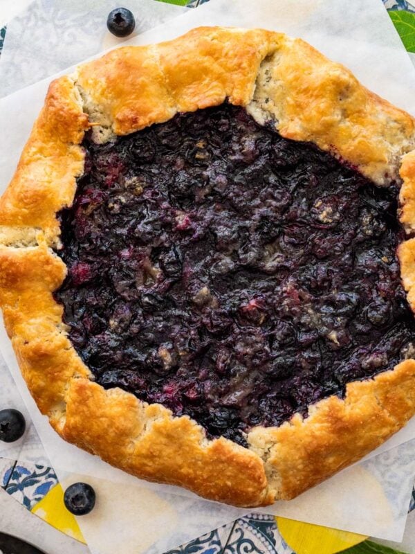 blueberry galette on two squares of parchment paper with fresh blueberries.
