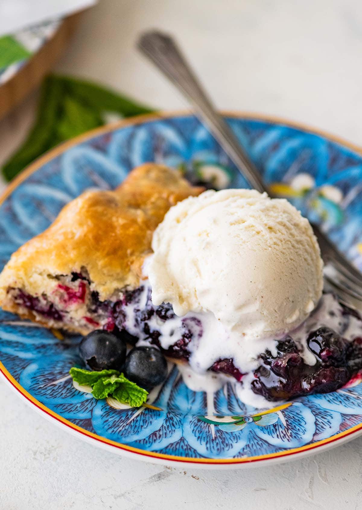 scoop of vanilla ice cream melting on top of a slice of blueberry galette.